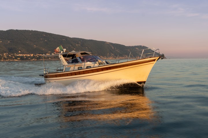 Motorboat cruising on calm water at sunset with hills in the background.