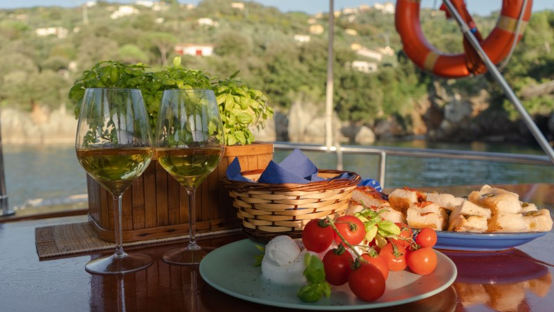 Two wine glasses, basil plant, tomatoes, bread on a table with scenic background.