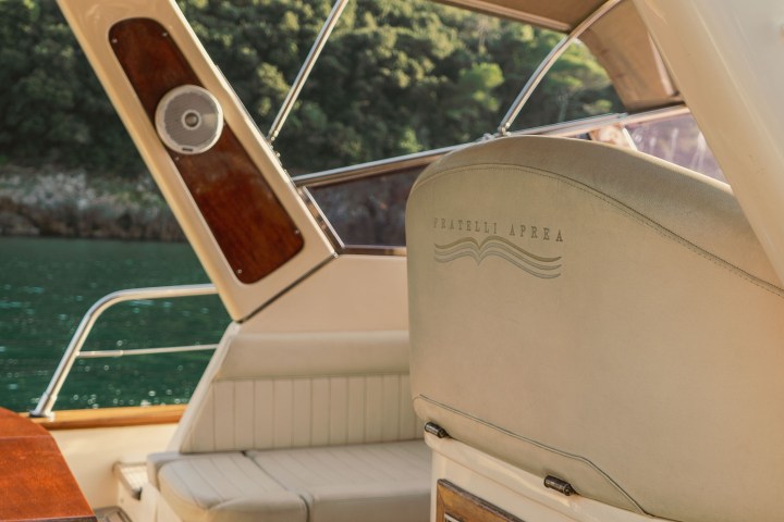 Boat interior with cushioned seating and wooden accents, overlooking the water with trees in the background.