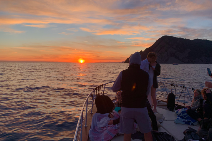 People on a boat watching the sunset with mountains in the background.