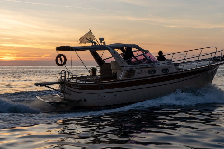 Boat cruising on the sea at sunset with a flag flying.