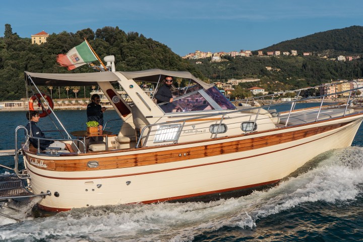 A motorboat with Italian flag cruising on water near a lush green coastline.