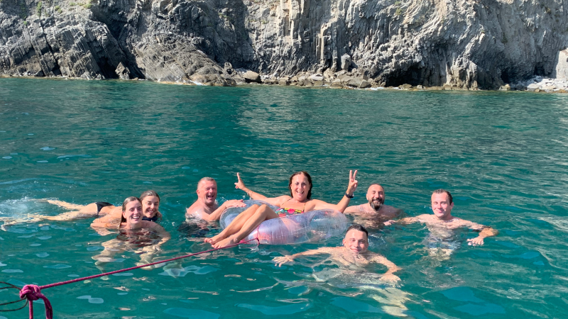 Group of people swimming near rocky cliffs, with one person on an inflatable tube.