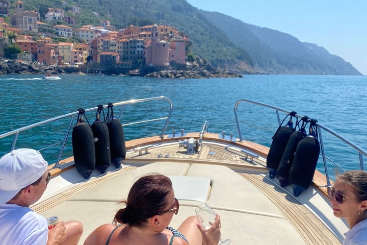 Three people relaxing on a boat with coastal town and hills in the background.