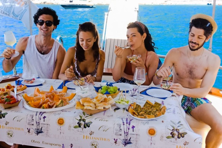 Four people enjoying a meal on a boat with a scenic ocean view.