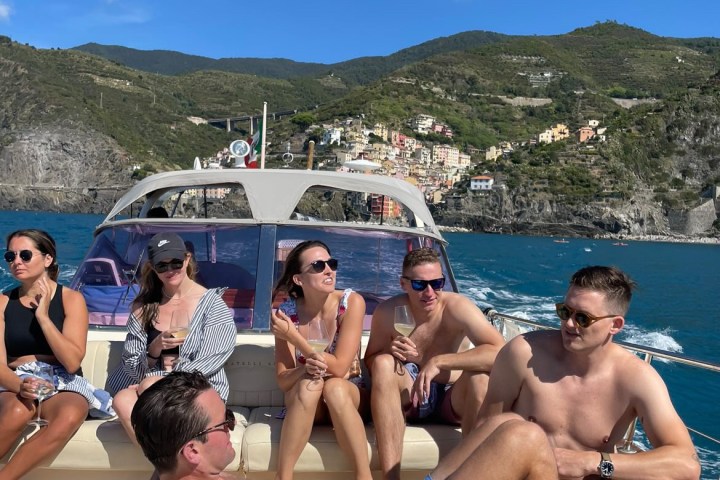 Group of people relaxing on a boat with coastal hills and blue sky in the background.