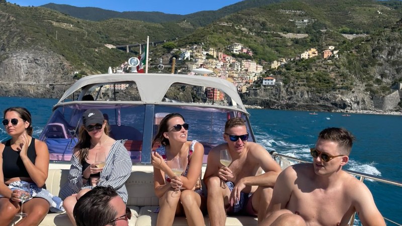 Group of people relaxing on a boat with coastal hills and blue sky in the background.
