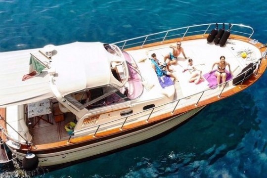 People sunbathing on a boat in clear blue water viewed from above.