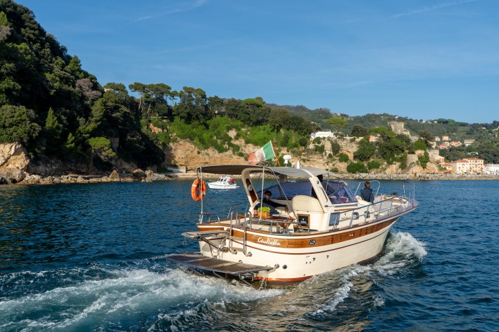 A boat sailing on the sea near a mountainous coast with houses and trees.