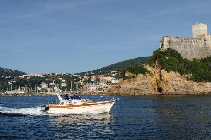 Boat on water with castle on rocky hill in background under clear blue sky.