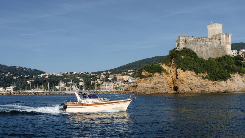 Boat on water with castle on rocky hill in background under clear blue sky.