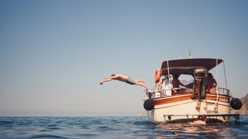 Person diving off a small boat into the ocean under a clear blue sky.