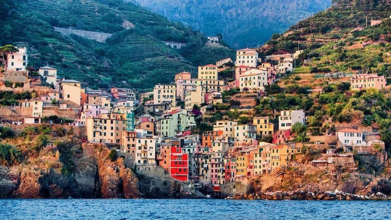 Colorful hillside village by the sea, surrounded by lush greenery and mountains.