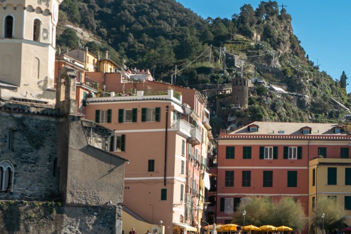 Vernazza harbor with colorful buildings, a boat, and hills in the background under clear sky.