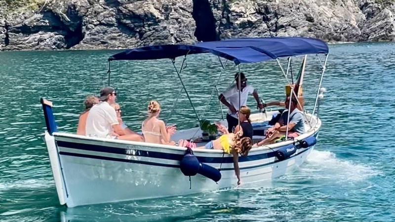 People relax on a small boat with canopy near rocky cliffs.