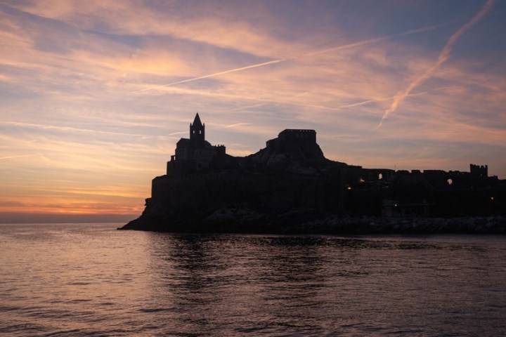 Silhouette of a fortress against a colorful sunset over a calm sea.