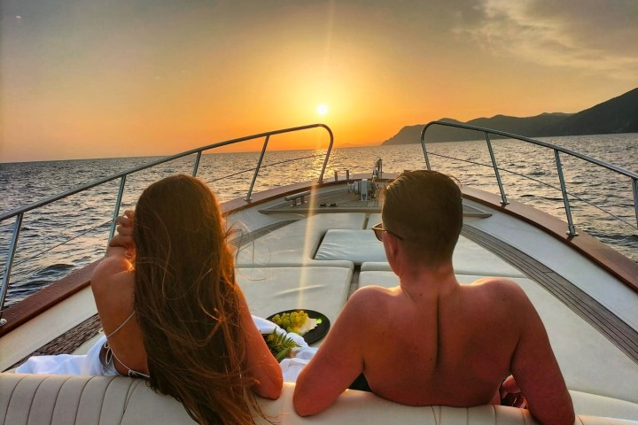 A couple relaxes on a yacht deck, watching the sunset over the ocean.