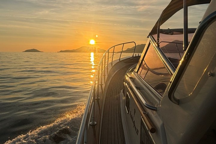 Boat sailing at sunset with distant islands and calm sea.