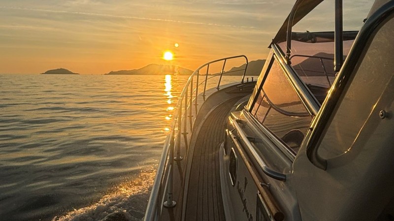 Boat sailing at sunset with distant islands and calm sea.