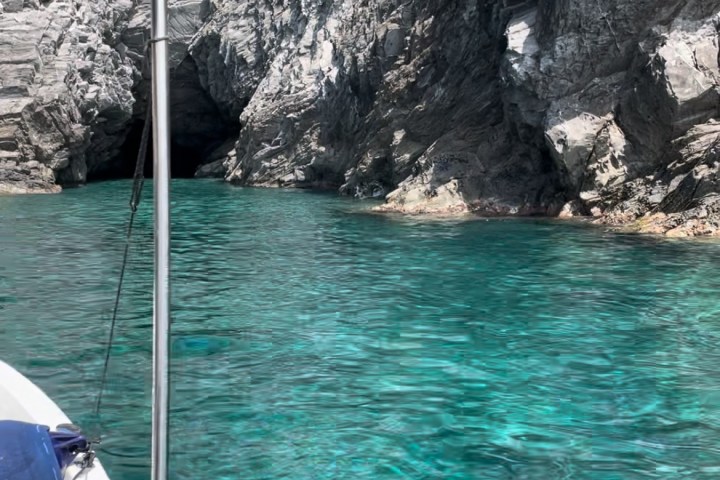 Boat near rocky cliff and clear turquoise water, with a cave entrance visible.