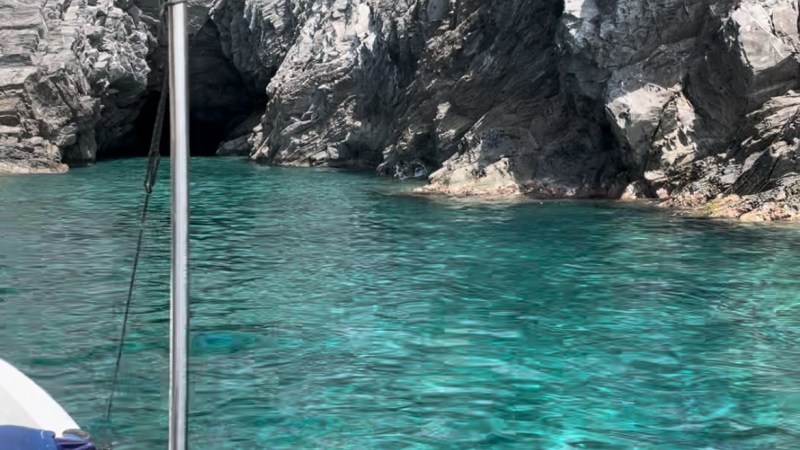 Boat near rocky cliff and clear turquoise water, with a cave entrance visible.