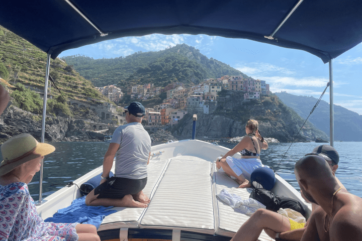 People on a boat approaching a coastal village with colorful houses on a hillside in the background.