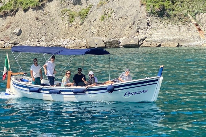 People on a small boat named 'Princess' with canopy, near rocky coast and calm blue water.