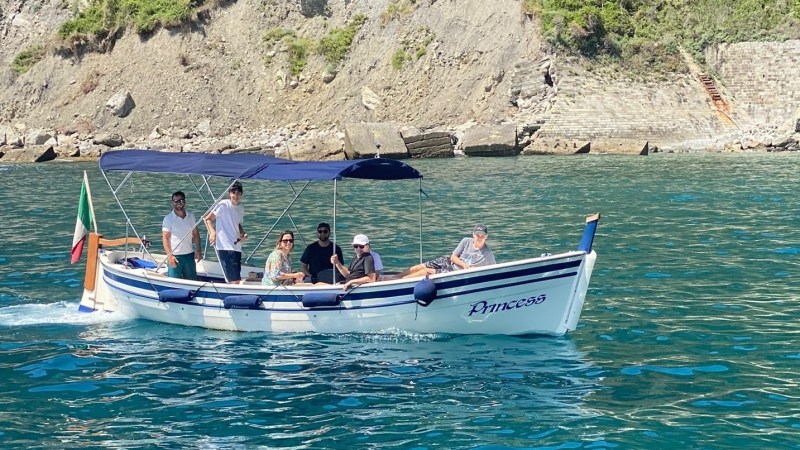 People on a small boat named 'Princess' with canopy, near rocky coast and calm blue water.