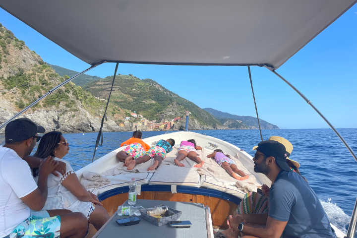 People relaxing on a boat near a rocky coastline under a clear blue sky.