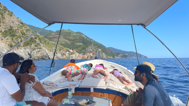 People relaxing on a boat near a rocky coastline under a clear blue sky.