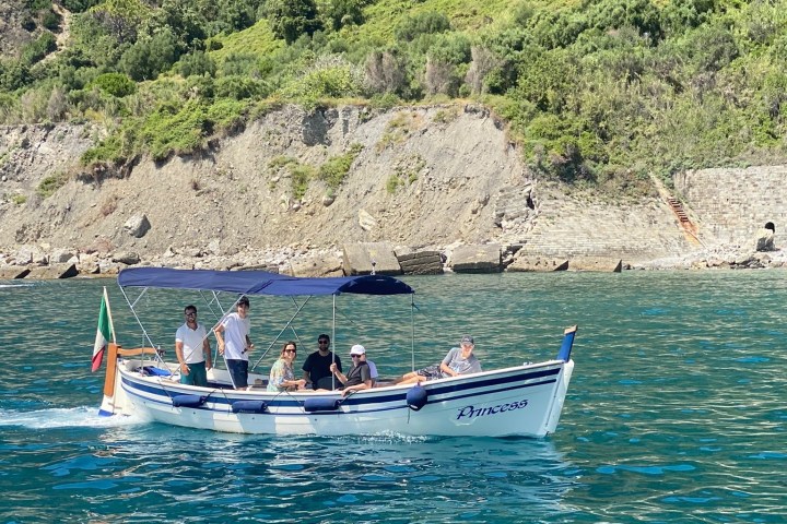 Group of people on a small boat with canopy near a rocky, green hillside.