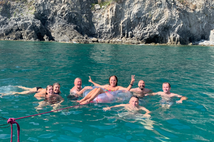 Group of people swimming near rocky cliffs in clear blue water, one person on an inflatable ring.