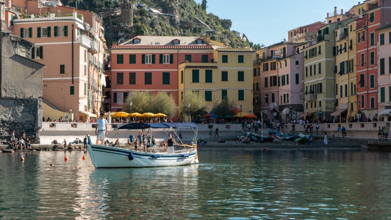 Colorful buildings by a waterfront with a boat and people on the shore.