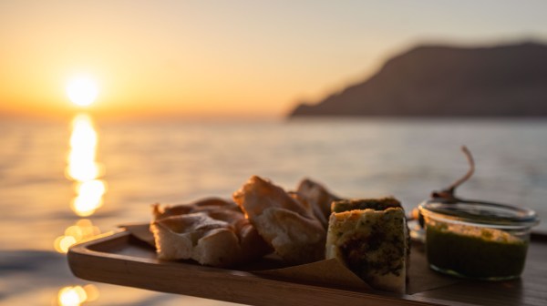 Tray with bread and pesto at sunset over the sea with mountains in background.