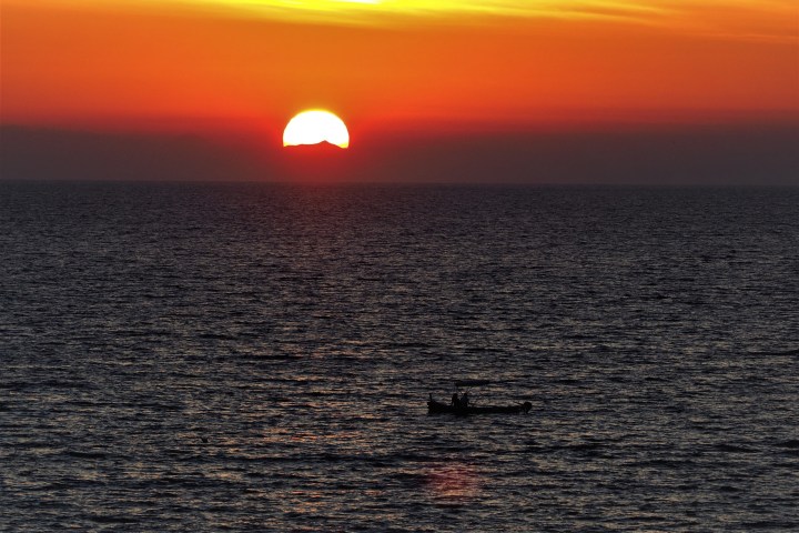 Sun setting over ocean with small silhouette of a boat in foreground.