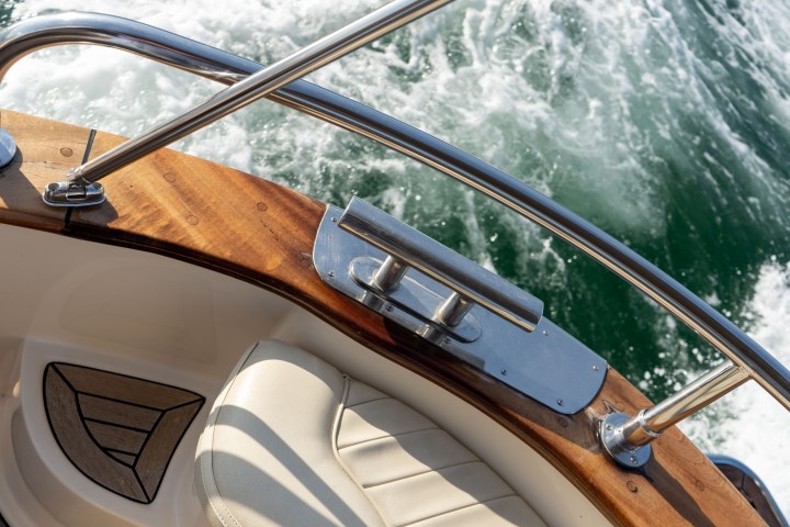 Boat interior with wooden railing, metal cleat, and water splashing at the stern.