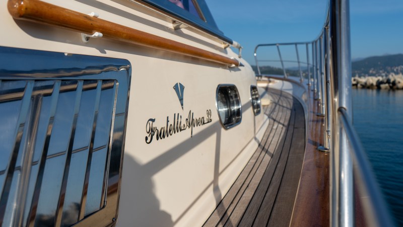 Close-up of a yacht's deck with railing, wood trim, and logo inscription.