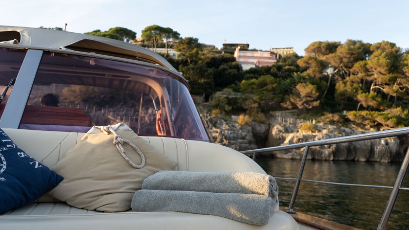 View from a yacht's seating area with cushions and towels, cliffs and trees in the background.