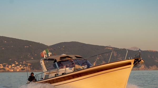 Motorboat speeding on water with hills in the background at sunset.